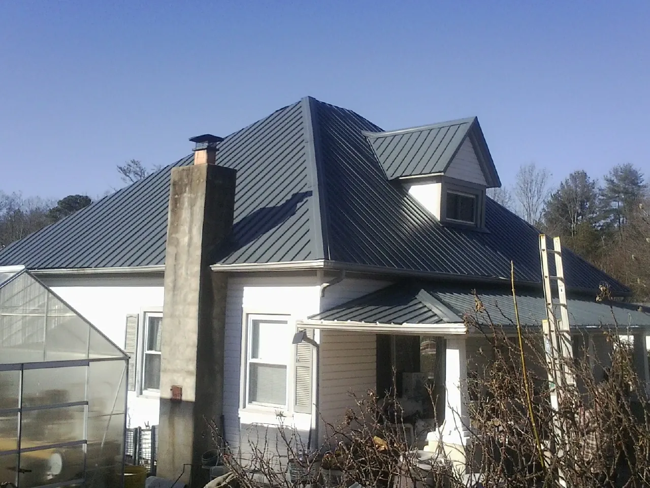 Dark blue standing seam metal roof on a white farmhouse with dormer — Slate & Tile Roof Repair by Roofing Brothers in Mannington