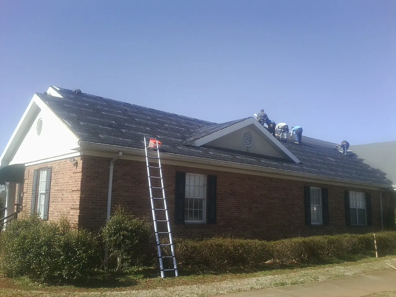 Crew tearing shingles off a brick ranch roof with a ladder set — Emergency Roof Repair work by our crew in Mannington