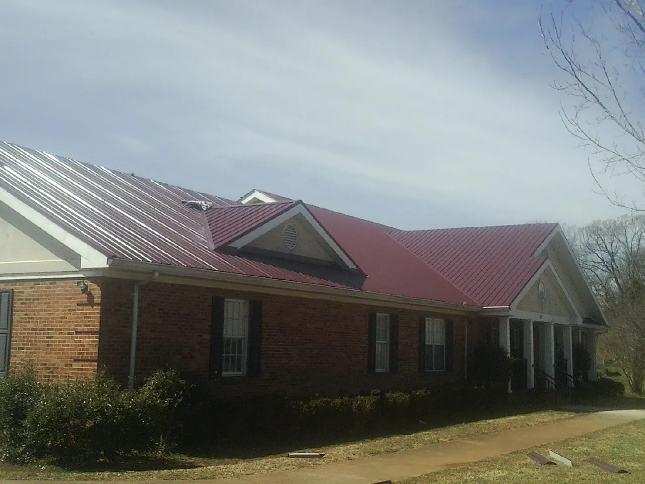 Red metal roof with gabled entries on a long brick building, from a Hail Damage Roof Repair job in Mannington