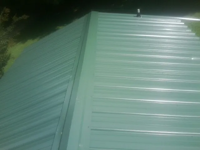 New green metal panels meeting at the ridge of a roof — Flat Roof Repair work by our crew in Mannington