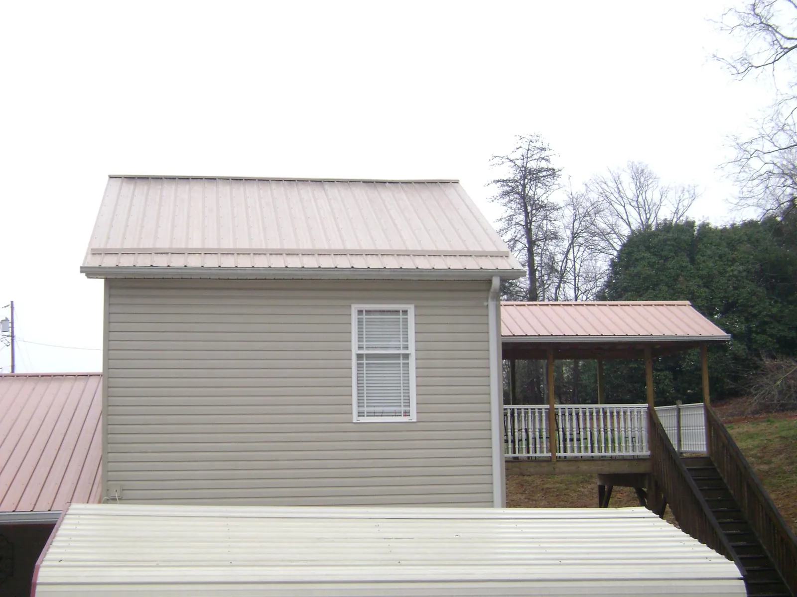 Tan metal roofs on a two story addition and attached porch, from a Roof Replacement job in Mannington